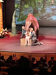 Two performers on stage reacting to a large, fantastical creature puppet during a theatrical production at Erth's Dinasour Zoo.