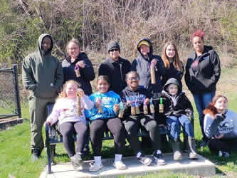 A group of parents, staff and students at he Wild Things event smiling and posing together. Some holding handmade bird feeder crafts.