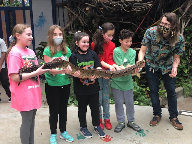 Group of students experiencing a hands-on learning moment with a large boa  constrictor snake at an educational event.