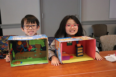 Two students displaying their creativity with colorful cardboard box dioramas.