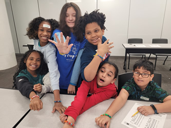 A group of cheerful children around a table showing their hands with colorful ink stamps on them, sharing a moment of fun and camaraderie.